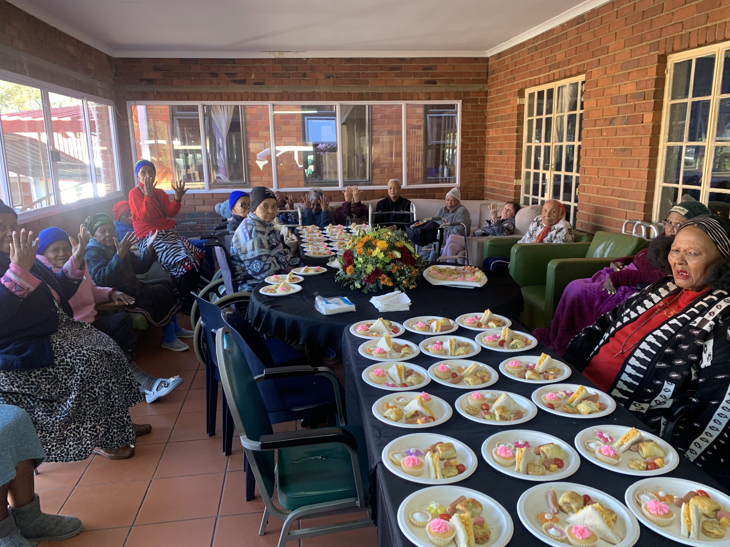 Residents at Frederic Place gathered around a table set with tea and treats for a celebration